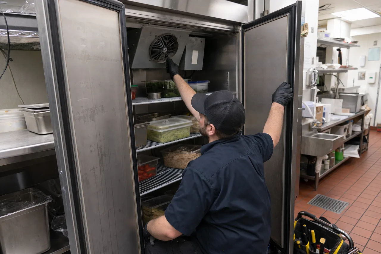 Technician servicing a commercial reach-in refrigerator up close